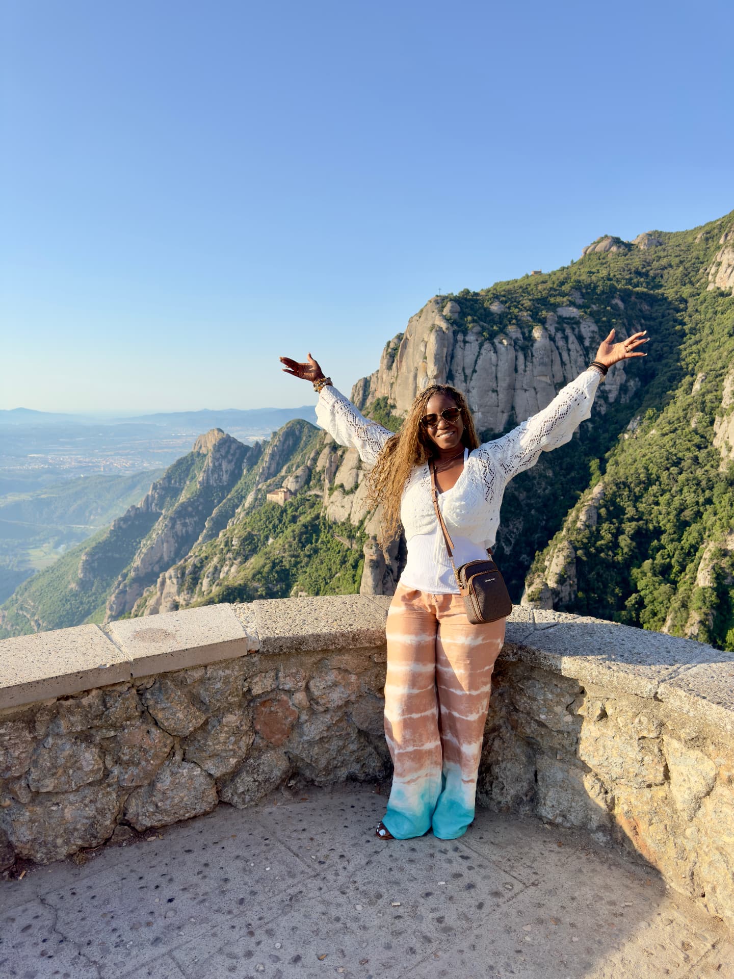 Sonya smiling with both arms raised at a mountain overlook in Montserrat, Spain